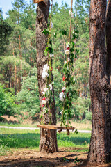 Wooden swing decorated with flowers and greenery between trees in a forest.