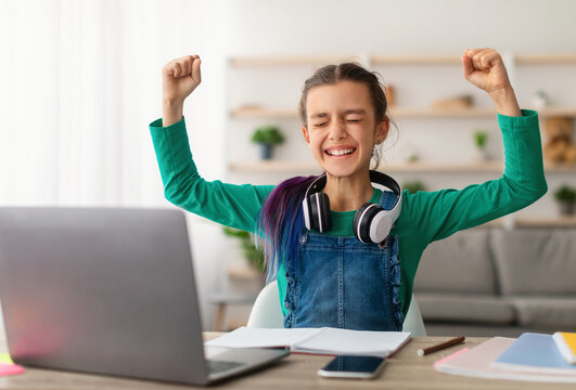 Little Winner. Excited Teen Girl Sitting In Living Room With Laptop Gesturing Yes Shaking Clenched Fists Getting A-Grade During Webinar At Home Celebrating Victory. Online School Tests Concept