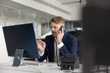 Serious hardworking business professional man talking on landline phone at office table, using...