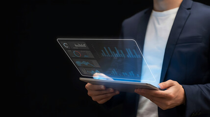 Businessman in a suit holding a futuristic holographic tablet displaying financial data and charts