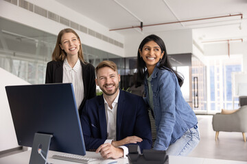 Multiethnic business team of happy young professionals sitting and standing at workplace, looking...