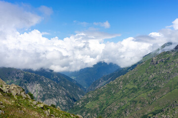Clouds enveloping green mountain peak under blue sky
