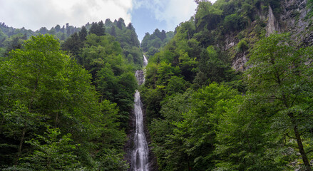 Scenic Tar waterfall cascading down rocky cliff into pond in lush green forest