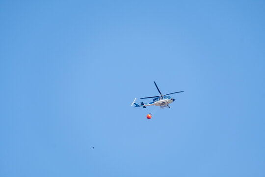 Plasencia, Caceres, Spain - August 16, 2025: Firefighting helicopter of the Spanish Governmen thovering above mountgainss, suspending large water bucket for combating active wildfire spread.