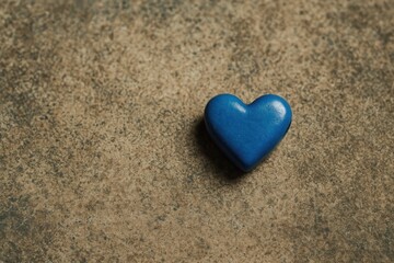 An azure-colored heart bead resting on the ground surface