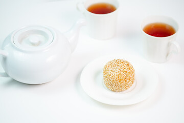 A single, golden sesame ball rests on a plate, presented with a teapot and two cups of warm tea for a simple and inviting moment of refreshment.