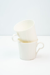 A clean and minimalist arrangement of two white porcelain teacups, artfully stacked on a seamless background.