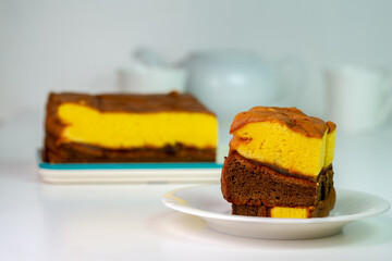 A delicious slice of a two-layer sponge cake with yellow and chocolate layers on a simple white plate. A classic, homemade sweet treat for any occasion.