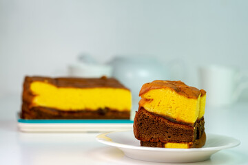 A delicious slice of a two-layer sponge cake with yellow and chocolate layers on a simple white plate. A classic, homemade sweet treat for any occasion.