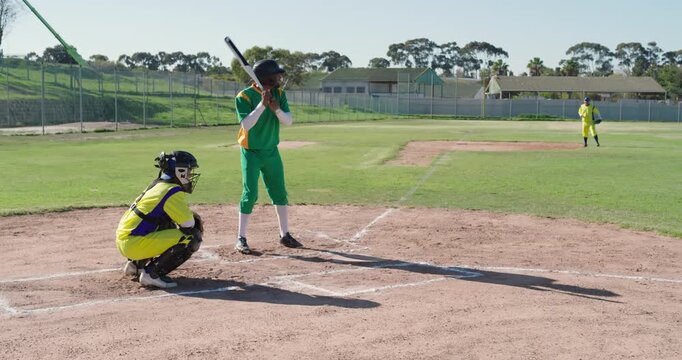 Pitcher delivering ball, African American man swinging bat, missing into mitt at baseball field