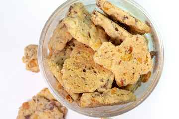 A top-down view of a clear plastic jar filled with delicious, crunchy almond cookies on a white background. Some cookies have spilled out, adding to the visual.