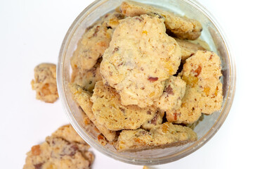 A top-down view of a clear plastic jar filled with delicious, crunchy almond cookies on a white background. Some cookies have spilled out, adding to the visual.