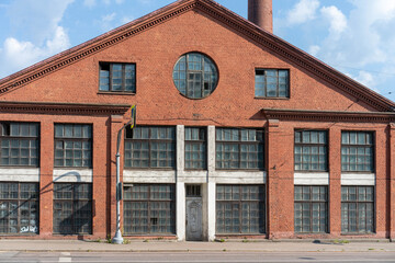 A large red brick factory building with multiple windows and a round window in the center