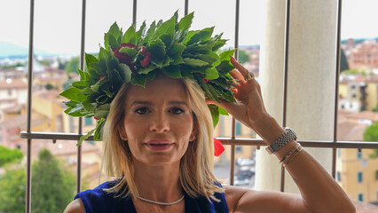 Joyful female graduate wearing laurel wreath celebrating on the Leaning Tower of Pisa