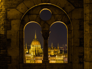 Budapest, Hungary &ndash; Night view of the illuminated Hungarian Parliament Building framed through the Fisherman&rsquo;s Bastion arch window.
