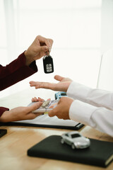 A car salesman hands over keys to a customer, symbolizing agreement, contract, purchase, rental, or...