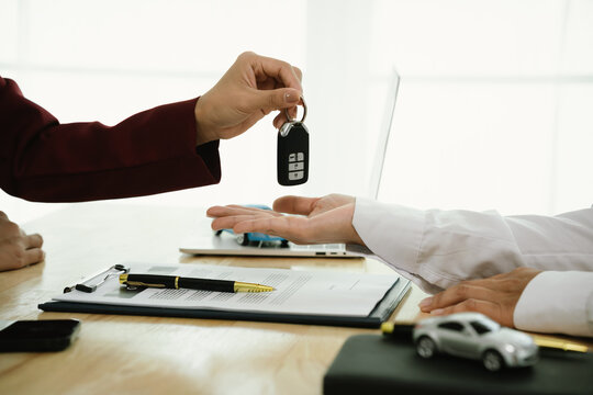 A car salesman hands over keys to a customer, symbolizing agreement, contract, purchase, rental, or insurance, representing finance, business, ownership, transportation, dealership service, and succes