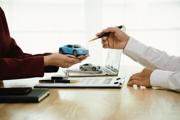 A car salesman hands over keys to a customer, symbolizing agreement, contract, purchase, rental, or...