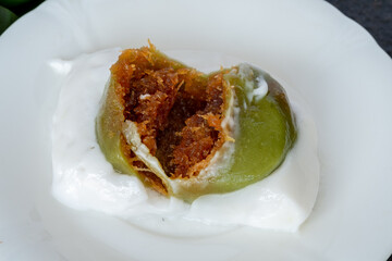 A sweet, traditional Indonesian cake called Kue Bugis Mandi, made of glutinous rice flour and coconut milk with a grated coconut filling, served on a white plate with coconut sauce. Lopis Ketan