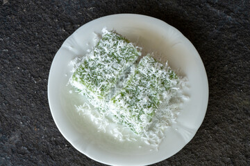 Two pieces of Ongol-Ongol, a traditional Indonesian sweet cake, made from sago flour or tapioca, with one piece on its side and another standing on its end, all covered in fresh grated coconut and ser
