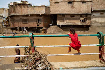 A girl sitting calmly on the safety railing by the riverbank, while the same river has destroyed...