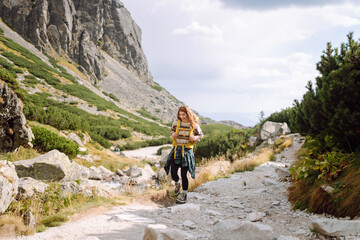 A female hiker with a yellow hiking backpack on a hiking mountain trail on a sunny day. Beautiful...