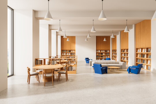 Modern library interior design with wooden bookshelves, round tables, and cozy blue lounge chairs in a spacious open reading area with pendant lights. 3D Rendering