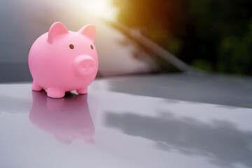 Pink piggy bank on a car hood represents saving money for car purchase, finance, investment, and...