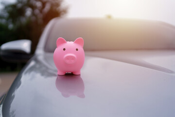 Pink piggy bank on a car hood represents saving money for car purchase, finance, investment, and...
