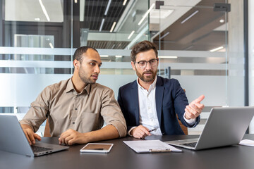 Colleagues collaborate in a modern office setting utilizing laptops and other digital devices for...