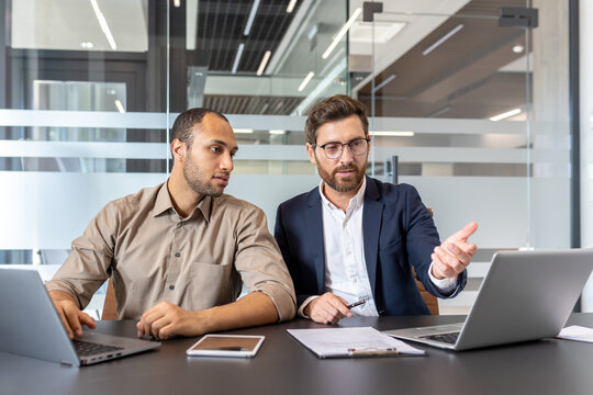 Colleagues collaborate in a modern office setting utilizing laptops and other digital devices for discussions. The image highlights teamwork, technology, and professional communication - Powered by Adobe