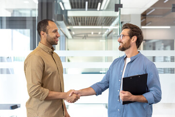 Two individuals engage in a handshake inside a contemporary office space, reflecting teamwork and...