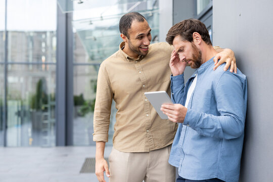 A supportive colleague comforts another while discussing something on a tablet in a modern office setting. - Powered by Adobe