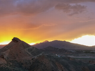 Naklejka premium Sunset over desert hills in Zhangye Danxia Scenic Area,China,dramatic sky over silhouette mountains,orange clouds,twilight glow,wilderness destination,peaceful dusk