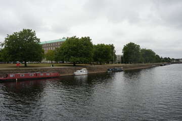 Nottingham Princess, England - August 16 2025: Mooring boats line the River Trent embankment with trees and council building under overcast light.