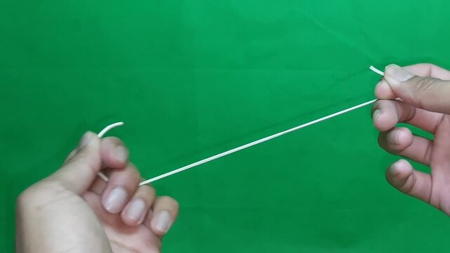 Close-up of a person stretching a rubber band to test its elasticity against a green screen background, perfect for flexibility, durability, and experiment concepts.