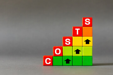 Increasing production and labor costs, rising raw material prices. The word COSTS on wooden blocks with arrows pointing up. Inflation icon. copy space grey background