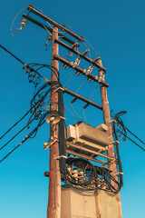 High-voltage electricity pole with power lines and transformer against clear blue sky. Utility...