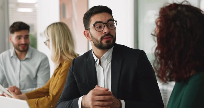 Young Arabian businessman lead dialogue with female partner or colleague seated at table in office, provide explanation, share opinion, working together on joint task or project. Business interaction