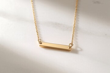 A close up of a gold bar necklace with a delicate chain on a white surface with soft lighting shown
