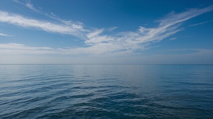 Obraz premium A serene view of calm blue waters under a bright sky with wispy clouds.
