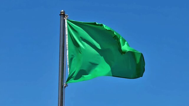 A vibrant green flag flutters gracefully and joyfully under a clear blue sky, symbolizing peace and prosperity for all