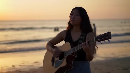Young woman playing guitar on beach at sunset