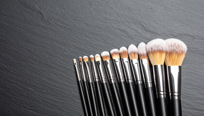 Makeup brush set with natural bristles arranged in neat row on dark textured surface, showcasing various sizes and shapes for detailed cosmetic application