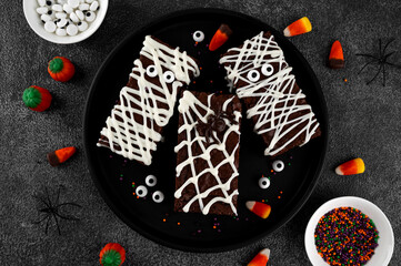 Halloween dessert. Chocolate brownie decorated with chocolate icing in the shape of a mummy and with a spider on a web. Top view, copy space.