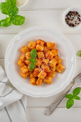 Traditional potato gnocchi with tomato sauce, parmesan cheese and fresh basil on a plate on a white wooden background. Italian cuisine. Top view, copy space.