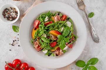 Salad with peaches, arugula, prosciutto, mozzarella cheese and cherry tomatoes with balsamic vinegar in a ceramic plate on a concrete background. Selective focus.