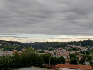Obraz premium Scenic cityscape under a cloudy sky. A tranquil view of a European town nestled among green hills. Perfect for travel blogs, editorial use or background. Serene and calming nature meets urban life.