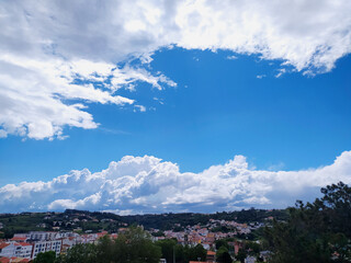 Bright, scenic vista of a town nestled under a dynamic blue sky filled with puffy white clouds....