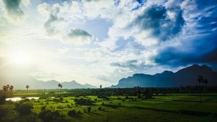 Sunrise over lush green fields in Aralvaimozhi, Kanyakumari, with dramatic clouds, distant...